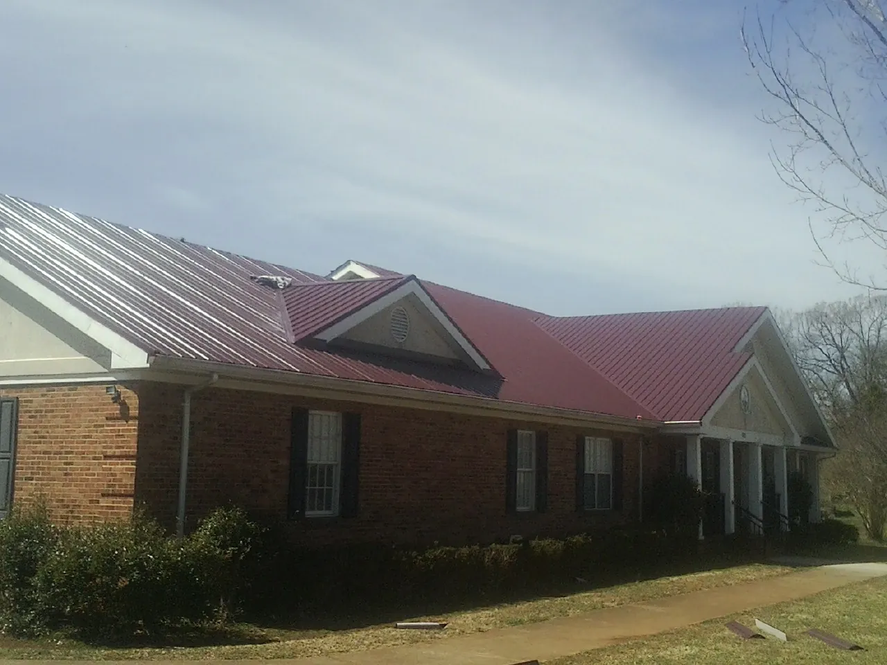 Red metal roof with gabled entries on a long brick building, from a Hail Damage Roof Repair job in Ellensburg