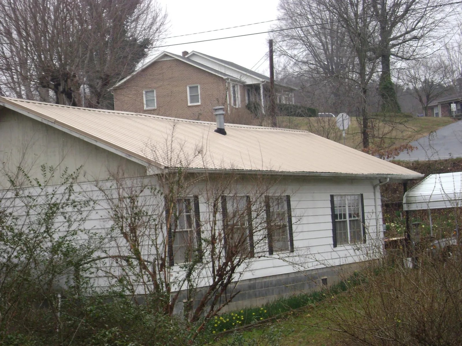 Tan metal roof on a white sided house set into a hillside — Commercial Roofing by Roofing Brothers in Ellensburg